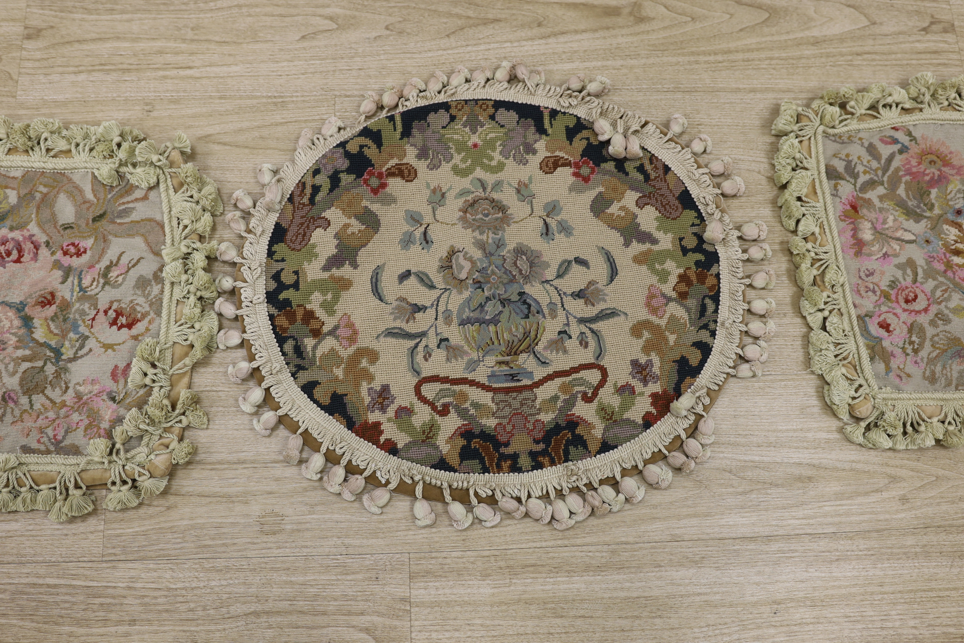 A pair or wool worked floral cushion covers with tasselled edging and an oval wool worked cushion with a floral petit point central cartouche, bordered with bobbling edging, oval cushion 57cm wide